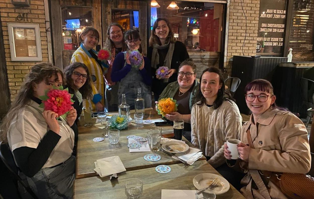 一群作家围坐在餐厅的桌子前微笑. 他们拿着纸花.