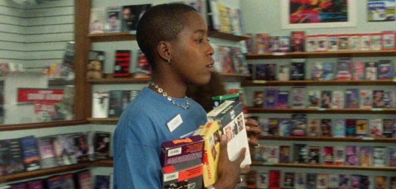 一个女人拿着一叠VHS录像带走过一家音像店