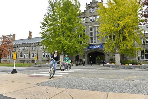Students riding bicycles in front of Pem Arch