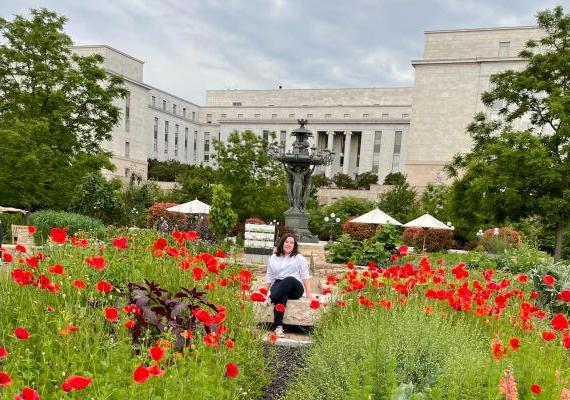 Zoe Balk seated outside amongst flowers with a building in the background