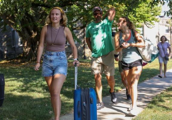 A dad and two students carrying bags as they move into the dorms