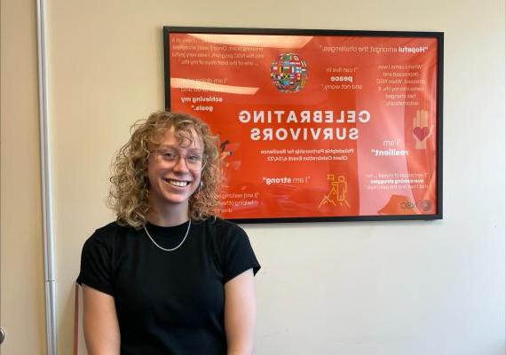 Emma Gross '25 poses in front of a "celebrating survivors" poster