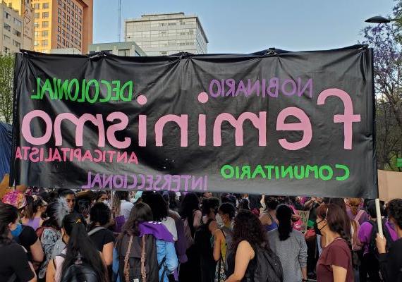 hand-painted banner reading "feminismo" held by women at an outdoor march