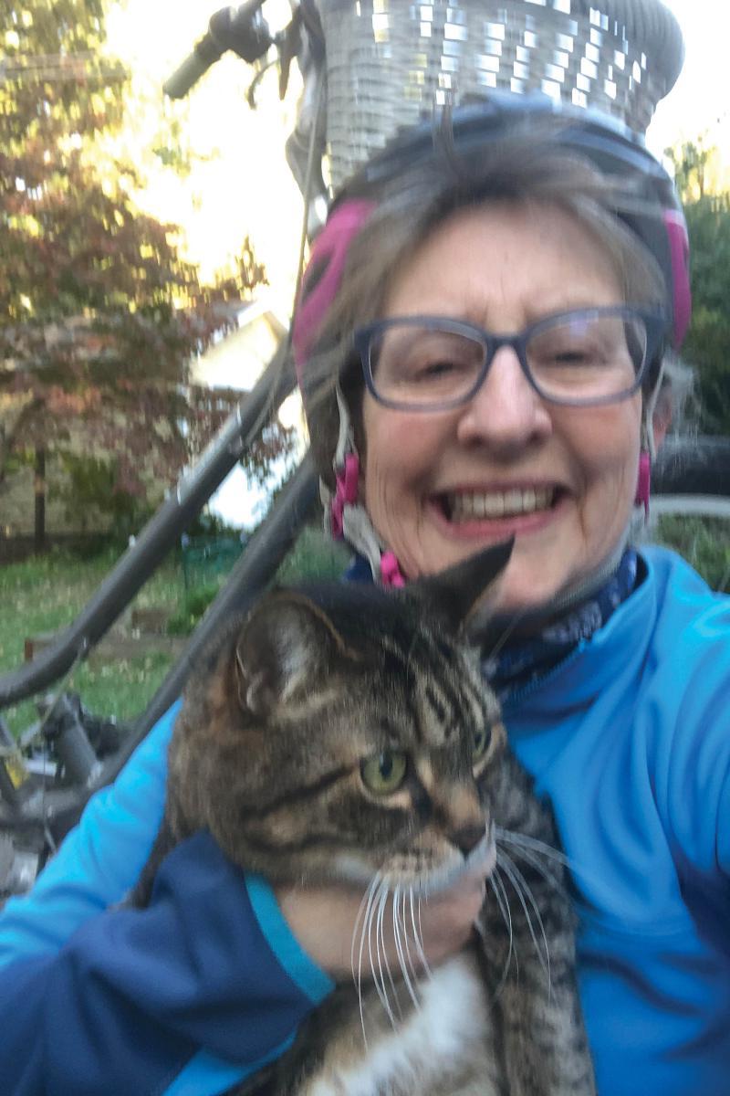 Portrait of Susan Burt wearing a bike helmet and holding a tabby cat.