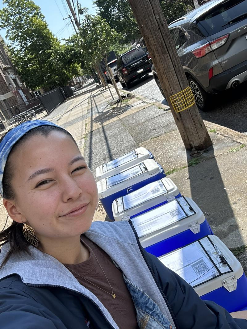 Amy taking a selfie amongst coolers on a street. 
