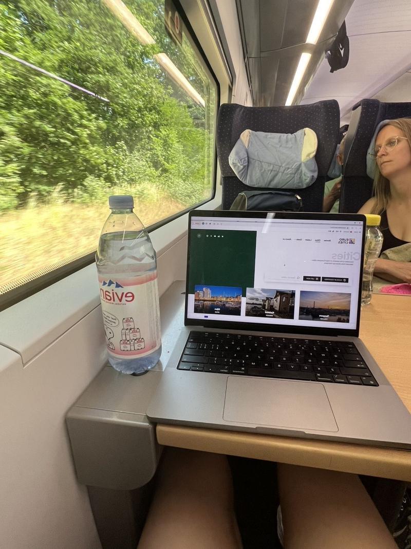 Train with a laptop and a water bottle on tray table. 