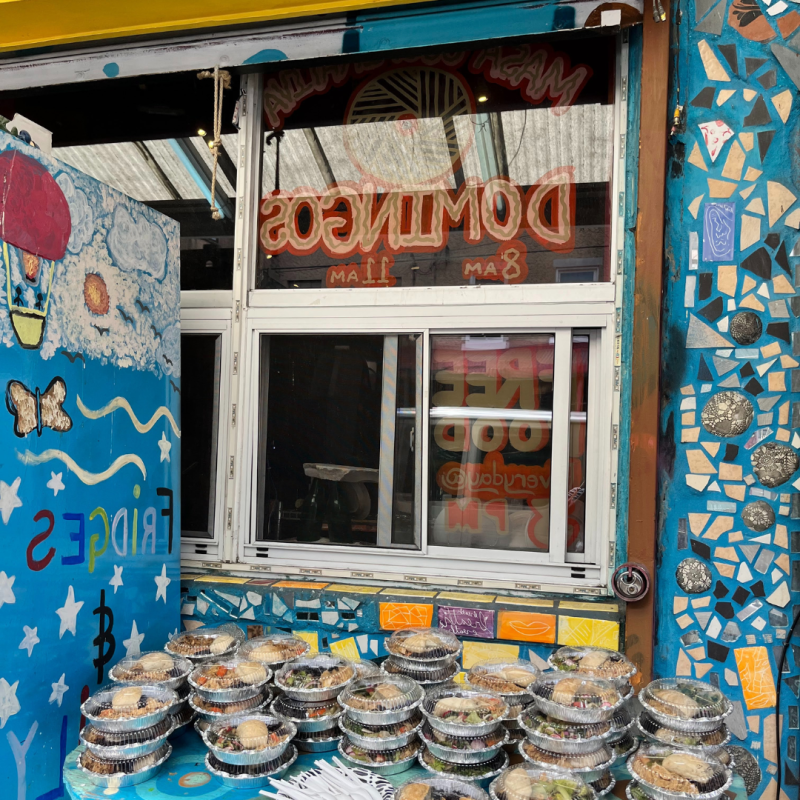 Restaurant pick-up window painted with a mural and a stack of take-out food containers. 